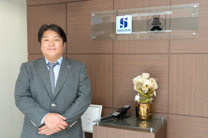 株式会社Kingmakerのロゴの前でインタビューを受ける株式会社Kingmakerの代表取締役の櫻井秀敏氏