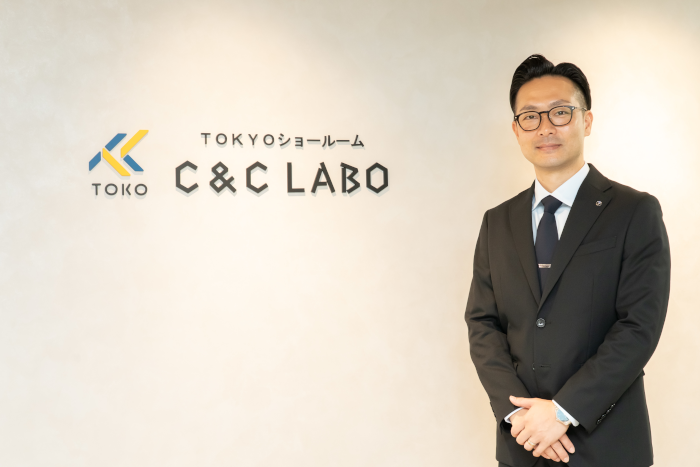 株式会社tokoのロゴの前に立つ取締役、佐々木祥氏